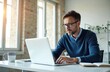 © Pete - Serious businessman working at office. Man with glasses types on laptop keyboard at desk. Professional works with concentration on computer. Business strategy is planned at workplace indoor.