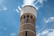 © LuIvDa - Torre de água histórica de formato cilíndrico, revestida a pedra e cimento, destacando-se contra um céu azul e algumas nuvens esparsas em Portugal
