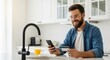© David - Cheerful handsome man with glasses and a beard holds a credit card and smartphone, enjoying easy online payment and e-commerce services in a modern home kitchen