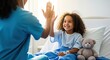© rdkcho - Happy little girl patient giving high-five to a medical professional in a brightly lit hospital room.