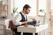 © Pixel-Shot - Young male writer with vintage typewriter, crumpled papers and books working at table in office