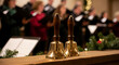 © val_webart - Golden hand bells on wooden table with choir performing in background