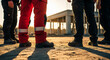 © Inspire Shots Hub - Low-angle view of industrial worker legs, wearing red and dark pants, plus work boots, standing on a construction site. Symbolizes labor, teamwork, progress