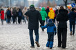 © K - Family in winter jackets walking along city street among crowd with child holding guardian’s hand on paved walkway during daytime urban movement scene