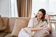 © SHOTPRIME STUDIO - Woman on sofa smiling and holding a glass of water in a bright livingroom, relaxed pose on a cozy couch, casual home interior scene conveying comfort and everyday relaxation.