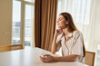 © SHOTPRIME STUDIO - Woman portrait at home, sunlight on table as she sits holding a glass in relaxation during morning. Cozy interior with curtains, thoughtful peaceful mood and natural bright light.