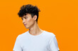 © SHOTPRIME STUDIO - young man wearing white t-shirt looks sideways with thoughtful expression against vibrant orange background in casual style portrait
