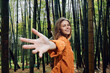© SHOTPRIME STUDIO - Woman smile bamboo forest hand reaching toward camera, portrait of happy young woman outdoors in nature wearing orange jacket, looking back and inviting viewer on a woodland walk.