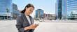 © insta_photos - Young happy Asian business woman wearing suit holding mobile phone standing in big city on busy downtown street, smiling lady using smartphone for texting, using apps outside