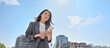 © insta_photos - Young Asian businesswoman wearing suit holding mobile phone standing in big city on busy downtown street. Young chinese business woman using smartphone texting, using apps outside