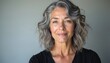 © Pete - Mature woman with wavy grey hair smiles gently against a plain background. Her calm expression and simple black top suggest confidence and inner peace. She embodies natural elegance.