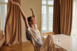 © SHOTPRIME STUDIO - Woman relaxed stretching in morning at home, sitting on chair by table with glass of water, casual clothes and peaceful expression, natural light and cozy interior