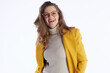 © Alliance - A cheerful professional woman with wavy brown hair and glasses smiles confidently in a bright yellow blazer and beige turtleneck against a clean white background.