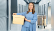 © Grispb - Storage facility services assist a woman organizing belongings, carrying a box through clean self-storage corridors with secured unit doors and carts.