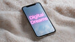 © Tetyana - Smartphone displaying digital dreams in glowing neon pink text on its screen, resting on a bed of sparkling glitter, illustrating modern technology, virtual reality, and digital escapism concepts