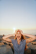 © SHOTPRIME STUDIO - happy woman enjoying sunset at the beach with rocky shore and clear sky, wearing denim shirt and red headband with joyful expression