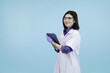 © Freddy Chandra - Smiling Asian female scientist or doctor in a lab coat and safety glasses, holding a tablet in studio blue background