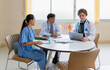 © chartphoto - Doctors and a nurse collaborate around a table reviewing digital patient diagnostics on a laptop during a modern clinical briefing session.