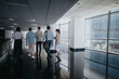© qunica.com - A diverse group of colleagues stroll through a bright, glass-walled corporate corridor.