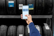 © cunaplus - Employee scanning a bar code on a tire at a garage shop using a cell phone.