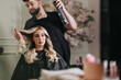 © qunica.com - A professional stylist shapes and curls a blonde client in a contemporary salon. Soft lighting, floral decor, and calm mood create a chic, beauty-focused atmosphere.