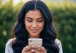 © Vasiliy - Smiling young woman using smartphone in a park. Happy brunette female texting on mobile phone outdoors. Technology and communication concept