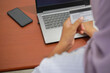 © tuan12 - Top view of a woman holding a credit card, blurred in the foreground, with focus on laptop keyboard and smartphone on a brown desk, copy space included for design