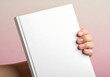© maikal - Hand holding a blank white book against a soft pink background