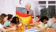 © JackF - Woman teacher tells pupils about Spain in a history lesson and holds the national flag of the country