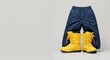 © Vyatcheslav - Yellow winter boots and blue snow pants on a gray background. Kids outdoor clothing for cold weather and snow activities. Banner with copy space for text