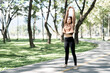 © NAMPIX - Asian woman stretching her arms overhead in a lush green park, enjoying a healthy outdoor workout.