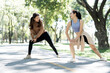 © NAMPIX - Two fit young Asian women performing lunges outdoors in a sunny park, focusing on exercise and healthy living.