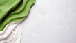 © AWAN - A top-down view of a textured white surface with a draped green fabric and a white fabric, creating a minimalist composition with soft lighting.