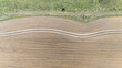 © AmazingAerialAgency - Aerial view of a sinuous dirt road carving through a field of muted gold, contrasting sharply with the vibrant green of the bordering vegetation, Paso de los Toros, Río Negro Department, Uruguay.
