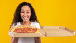 © Prostock-studio - A joyful young lady gazes at an open pizza box filled with tasty Italian pizza. She stands in front of a bright yellow-orange wall, celebrating her food delivery.
