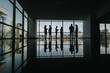 © qunica.com - Silhouetted coworkers stand in a spacious, glass-filled lobby, engaging in a casual conversation.