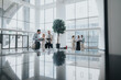 © qunica.com - A group of colleagues gather in a sunlit, glass-walled lobby, sharing tablets and ideas in a spacious corporate space that emphasizes collaboration and networking.