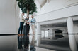 © qunica.com - Bright, contemporary lobby scene with three coworkers reviewing a project on a laptop, conveying collaboration, planning, and a professional, energetic mood in a sleek, reflective space.