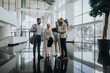 © qunica.com - A diverse group of people stands in a bright, glass-walled lobby examining a tablet together, signaling collaboration and teamwork in a contemporary corporate setting.