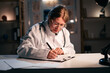 © Andrii Lysenko - Doctor woman in white coat writing notes in documents sitting at table in clinic during night shift