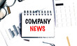 © Iryna - Company news phrase written on notepad with glasses, pen, charts and keyboard on white desk background