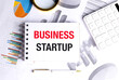 © Iryna - Business startup phrase on notepad with charts, calculator, magnifier and pen on white office table