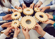 © Studio Romantic - Team of people connecting cogs. Group of men and women sitting in a circle and joining wooden gear wheels that they are holding in their hands. Teamwork, business, connection concept