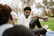 © Drobot Dean - A man holds a phone and smiles while sitting on a blanket and listening to his male friend next to him