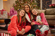 © SuperStock - Mother and two daughters wearing festive pajamas pose together in front of decorated Christmas tree