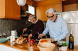 © Drobot Dean - A man holds a board with chopped vegetables while a male friend stirs a frying pan with a spatula next to him