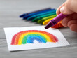 © Sasiwan - Hand drawing colorful rainbow with purple crayon on white paper, vibrant wax crayons in background, creative and cheerful mood, art activity for children, close up view