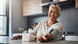 © Athiphat - Happy senior woman using smart blood pressure monitor at home, smiling and relaxed in modern kitchen, healthy lifestyle, independent living, wellness, technology for elderly