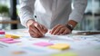 © Muhammad - Person writing on paper with pen surrounded by sticky notes and phone on a white surface