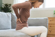 © KMPZZZ - Pain body muscles stiff problem, suffer asian young woman painful back, symptom injury ache from long study work, hand holding massaging or rubbing lower back hurt, sore sitting on sofa at home.